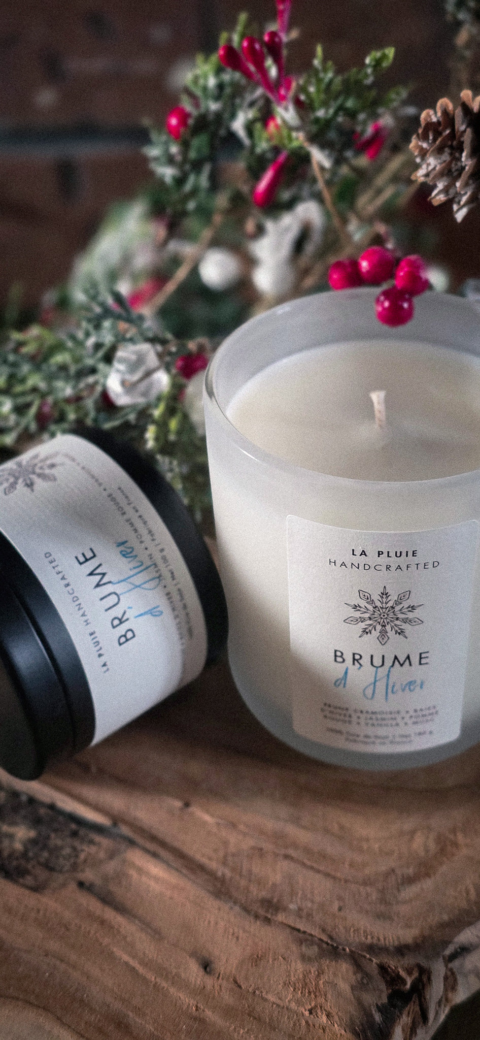 Candle and bottle labeled 'Brume d'Amour' on a wooden surface with festive decorations.