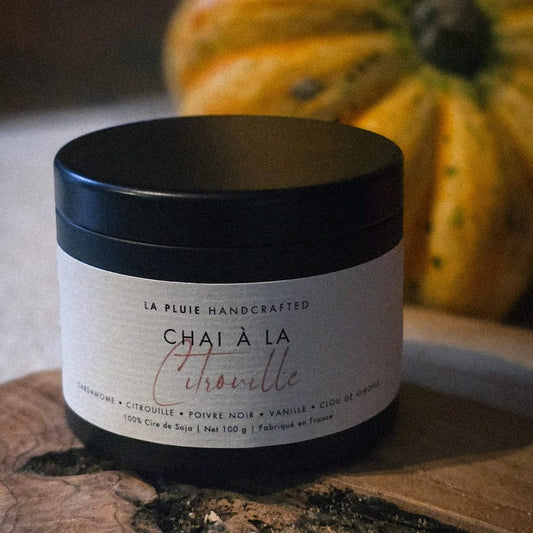 Jar of 'Chai a la Citrouille' on a wooden surface with pumpkins in the background